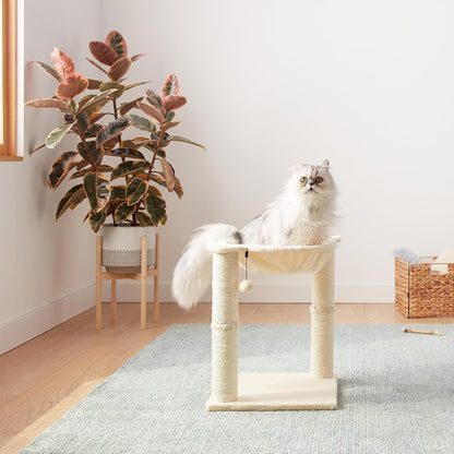 Cat lounging in beige hammock tower next to plant in cozy home setting